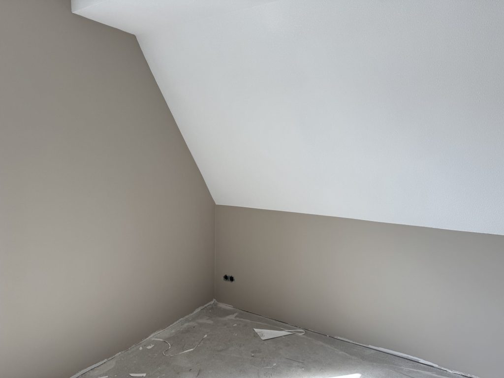 Zolderkamer met schuine wand, strak afgewerkt in een warme grijze tint met een wit plafond