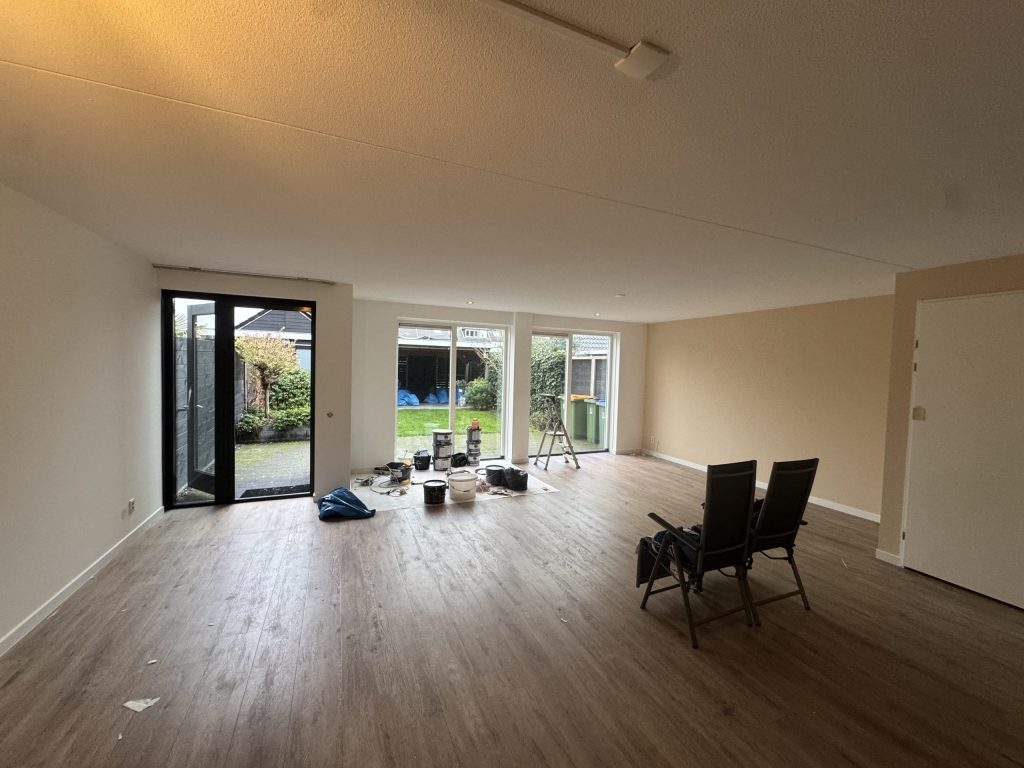 Lege woonkamer met lichte wanden, tuindeuren en verfemmers klaar voor het afwerken