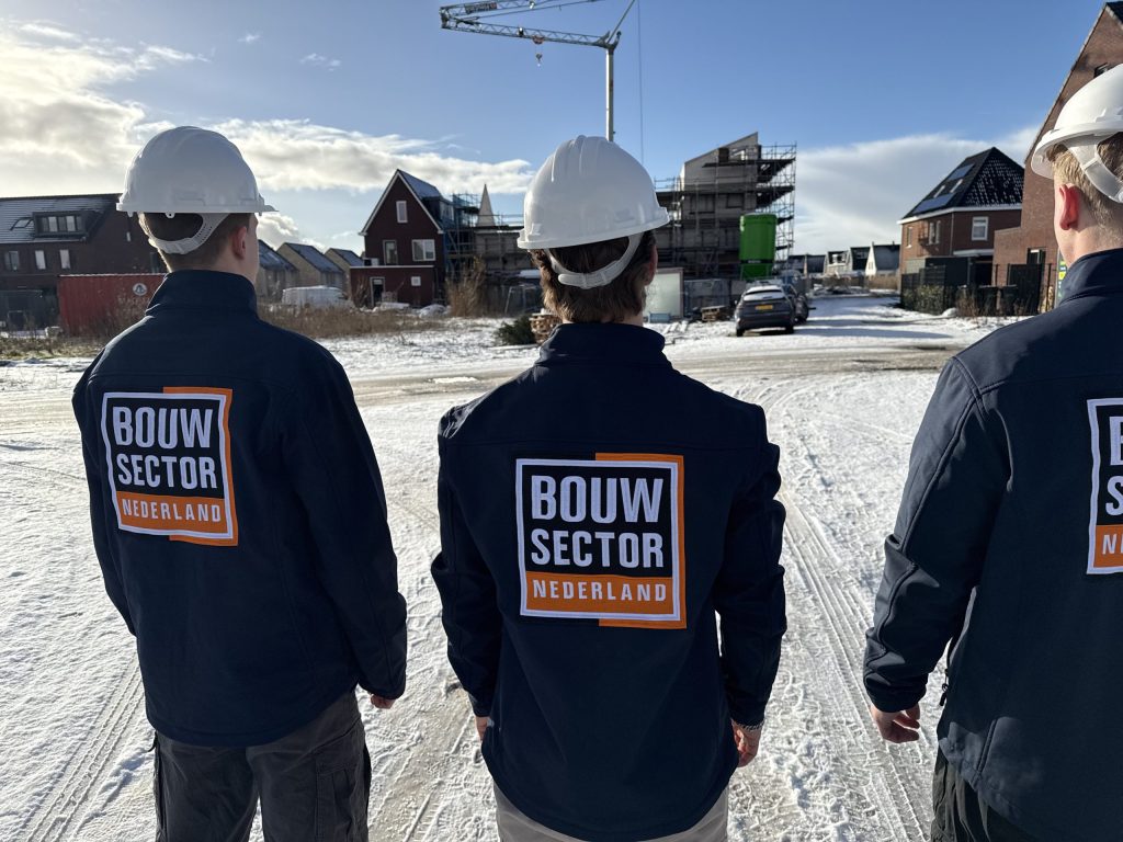 Drie vakmensen van Bouwsector Nederland met witte helm op een besneeuwde bouwplaats met een hijskraan